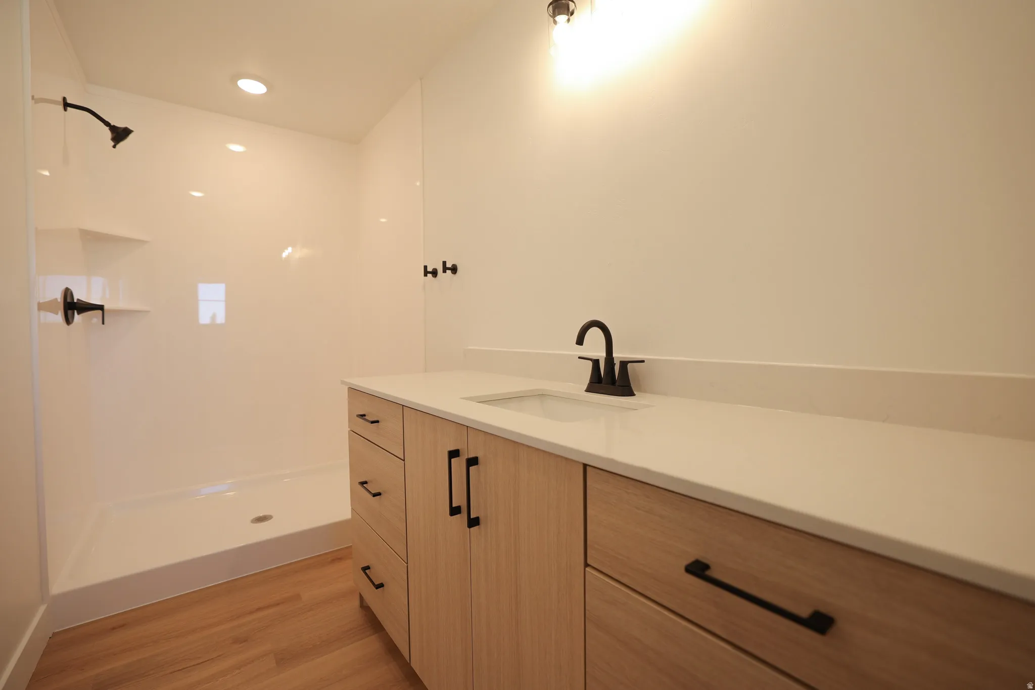 Hard-surface flooring, contemporary light wood-finish cabinetry, sleek countertop, integrated sink, and modern black fixtures