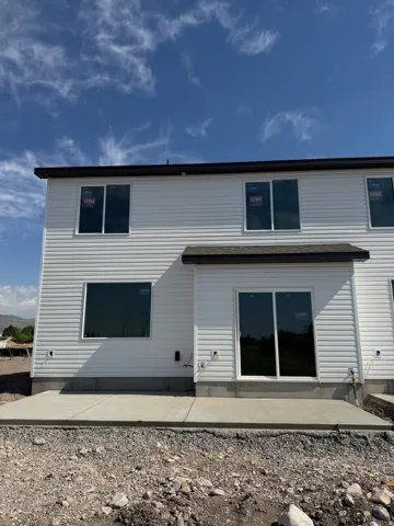 Rear exterior featuring white horizontal siding, a dark shingle roof, and a concrete patio
