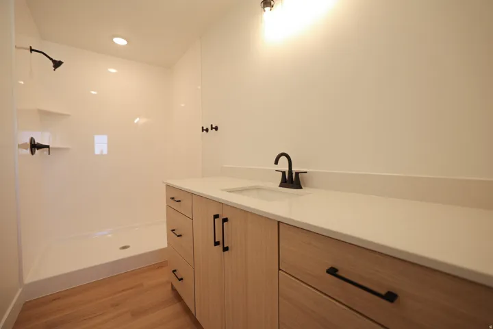 Hard-surface flooring, contemporary light wood-finish cabinetry, sleek countertop, integrated sink, and modern black fixtures