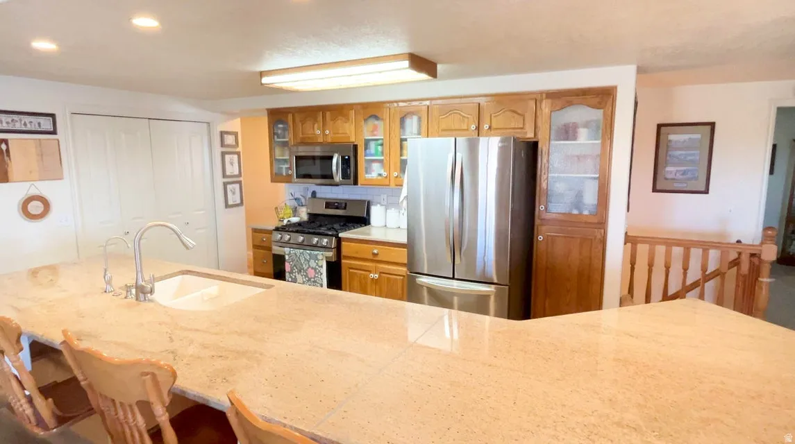 Kitchen with glass insert cabinets, stainless steel appliances, recessed lighting, wood finish cabinetry, and a kitchen bar