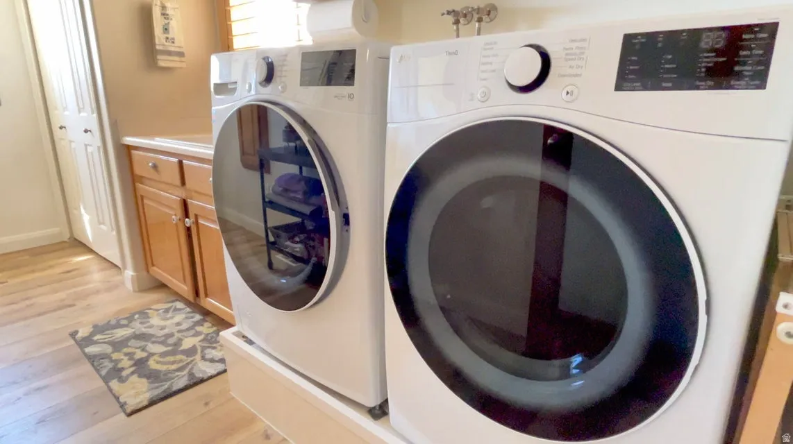 Laundry room featuring light wood-style flooring, washer and dryer, and cabinet space