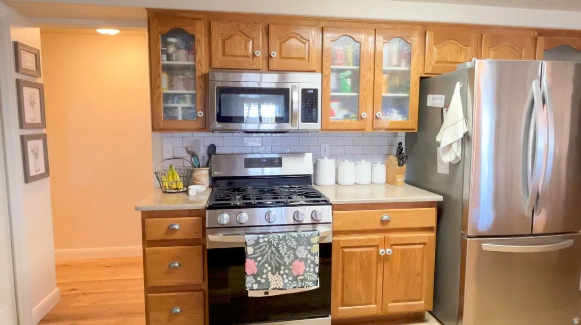 Kitchen featuring stainless steel appliances, glass fronted cabinets, and wood finish cabinets