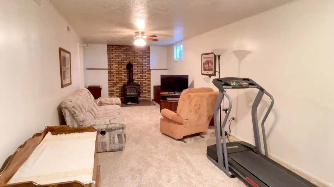 Exercise area featuring a textured ceiling, a wood stove, carpet floors, and ceiling fan