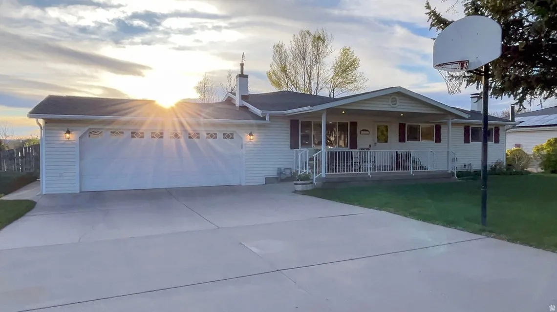 Ranch-style home with covered porch, a garage, a front yard, concrete driveway, and a chimney