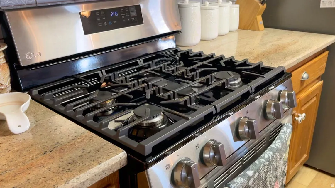 Kitchen view of stainless steel range with gas cooktop, light stone countertops, and wood finish cabinetry