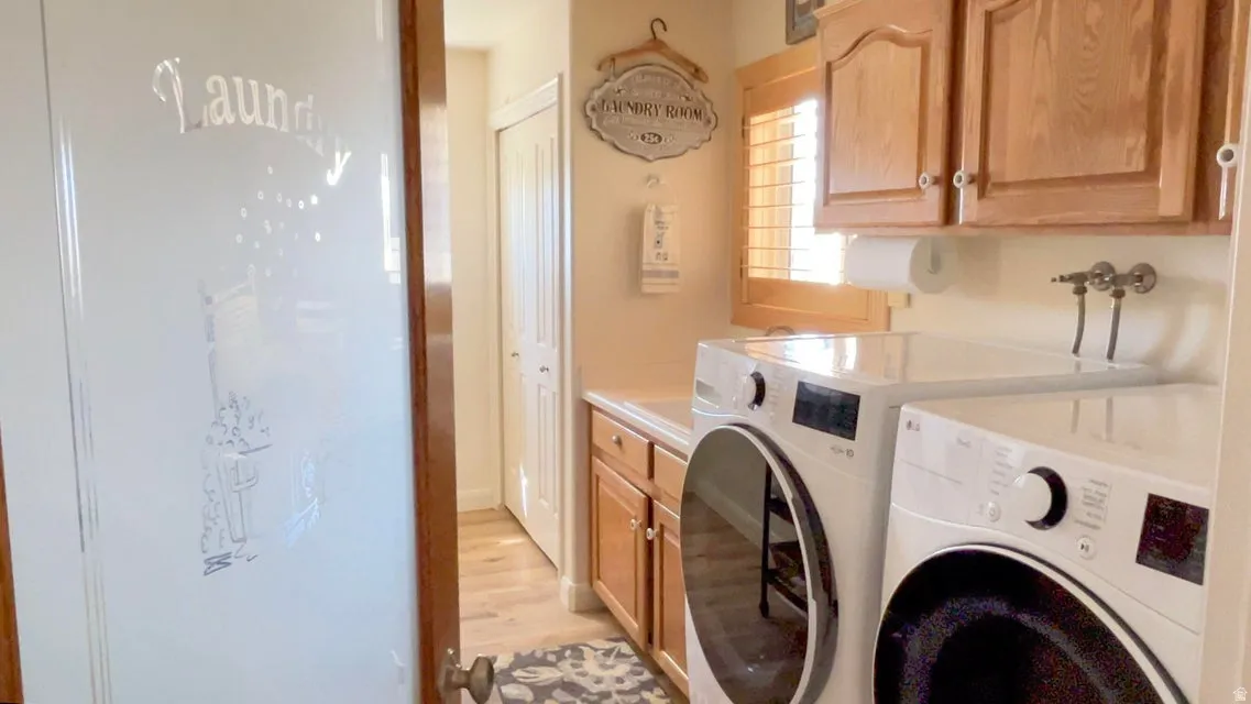 Laundry room with cabinet space, washing machine and dryer, and light wood-style flooring