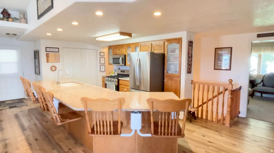 Kitchen with stainless steel appliances, a kitchen bar, light wood-style floors, recessed lighting, and glass fronted cabinets
