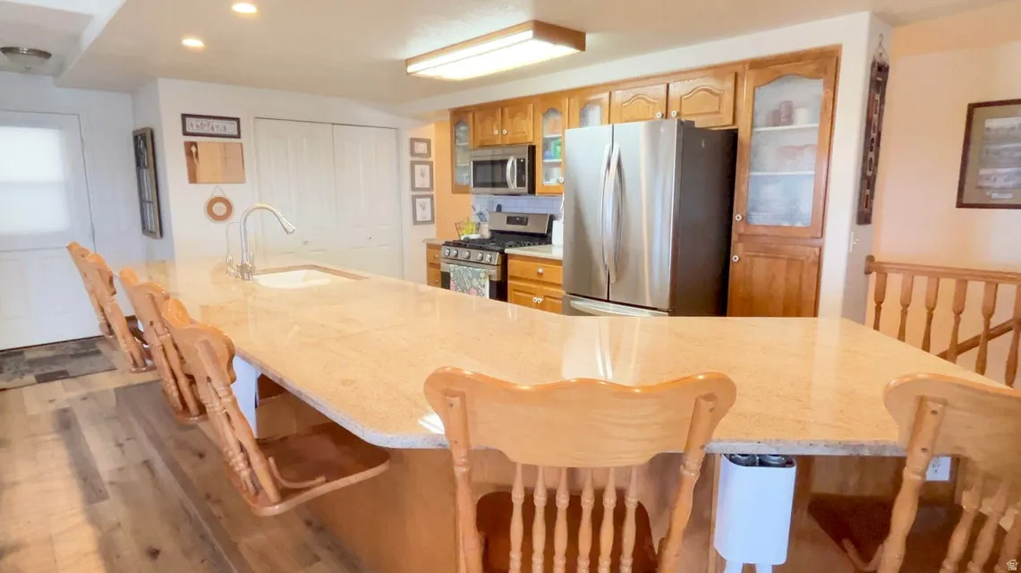 Kitchen with glass fronted cabinets, stainless steel appliances, a breakfast bar, wood finished floors, and recessed lighting