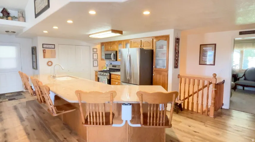 Kitchen with stainless steel appliances, a kitchen bar, light wood-style floors, recessed lighting, and glass fronted cabinets