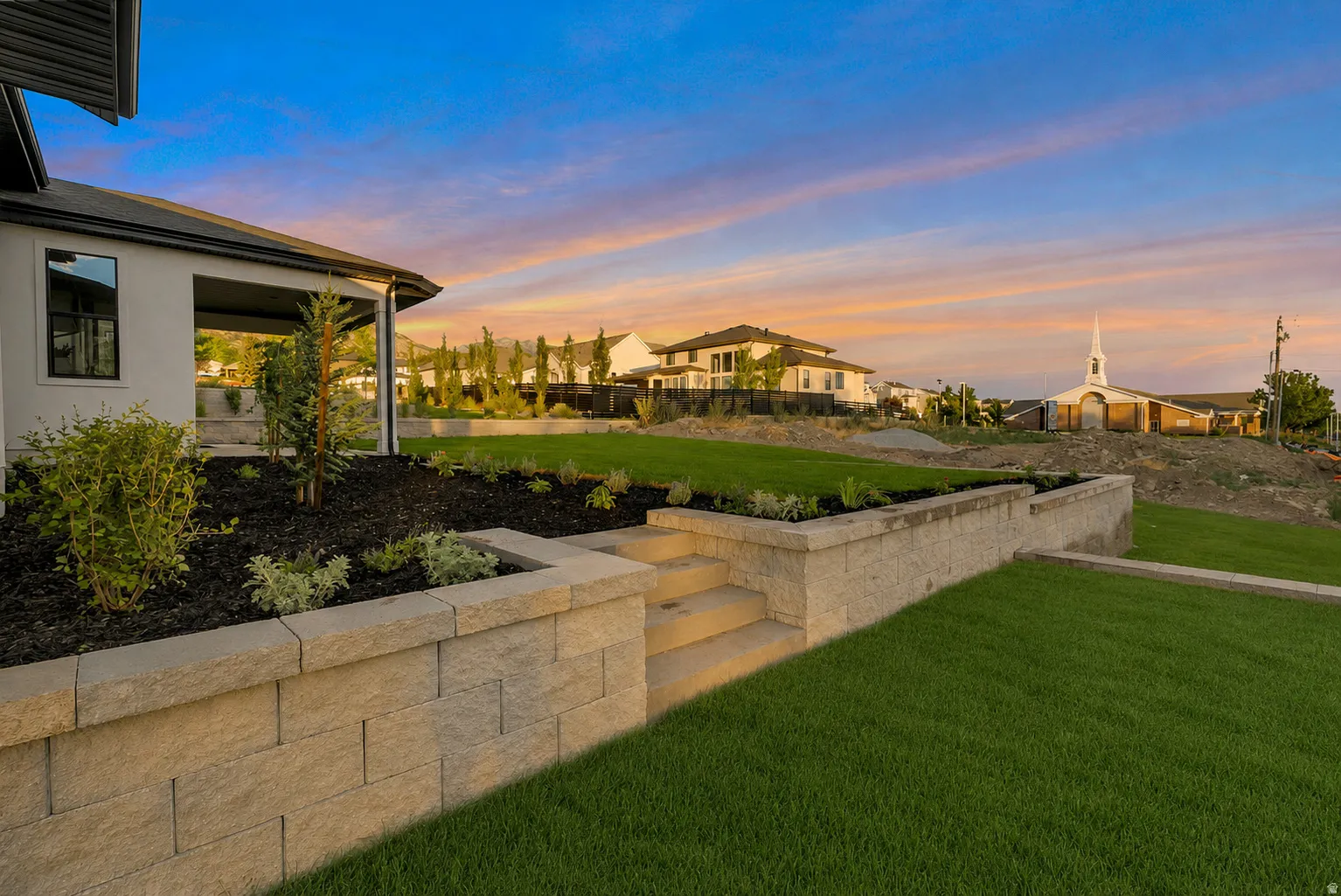 Spacious backyard featuring tiered landscaping with retaining walls, a manicured lawn, and planted garden beds