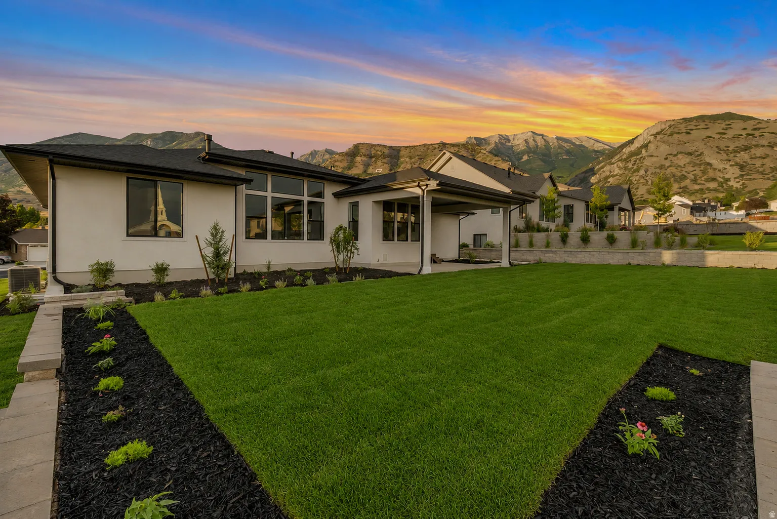 Expansive backyard featuring a manicured lawn, organized landscape beds, and a covered patio