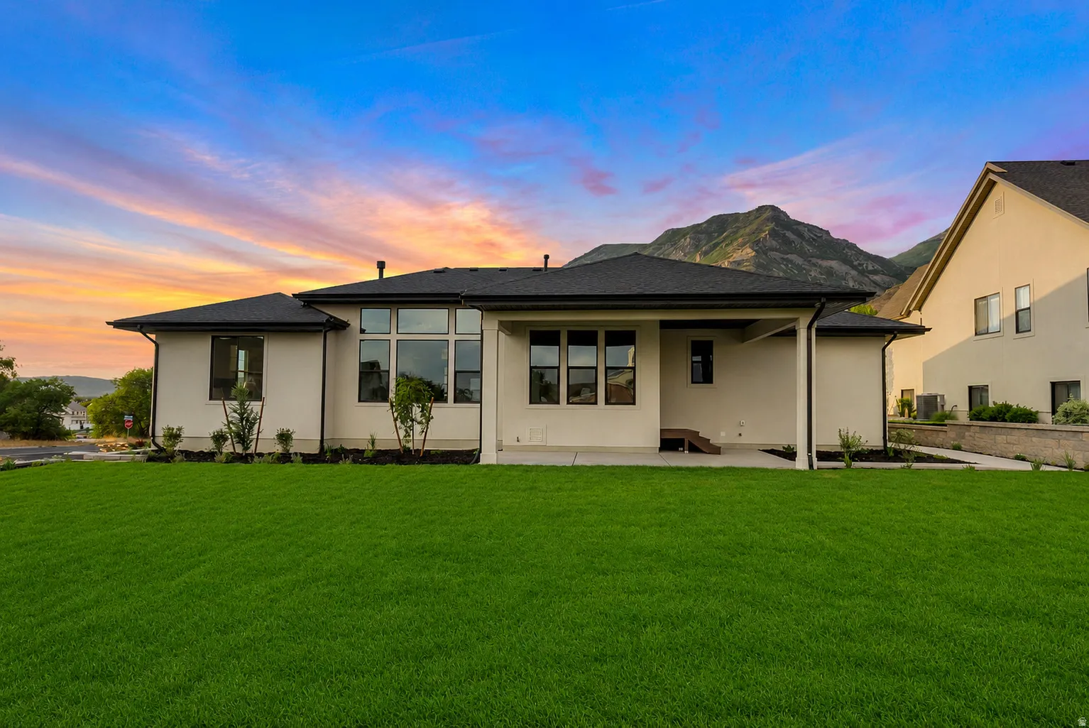 Expansive green lawn bordering a contemporary residence with a dark shingle roof, light-colored stucco exterior, and black-framed windows