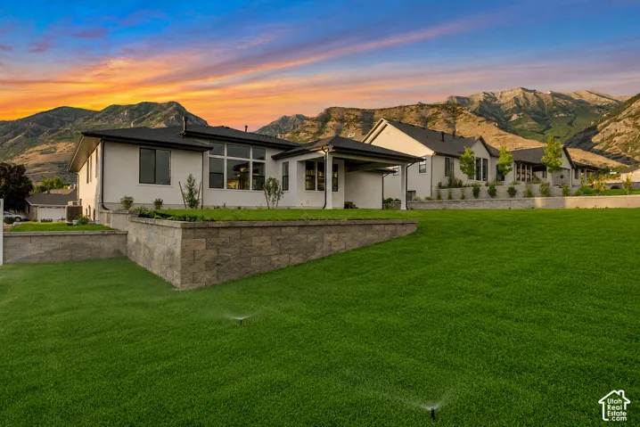 Expansive green lawn with visible irrigation system, retaining walls featuring stacked stone, and a modern stucco exterior with dark-framed windows