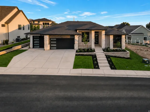 Modern residence featuring a stone and stucco exterior, a dark shingle roof, and a concrete driveway
