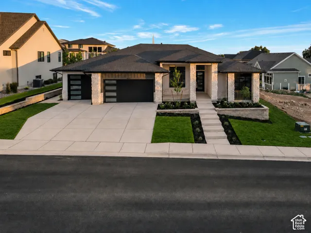 Modern residence featuring a stone and stucco exterior, a dark shingle roof, and a concrete driveway