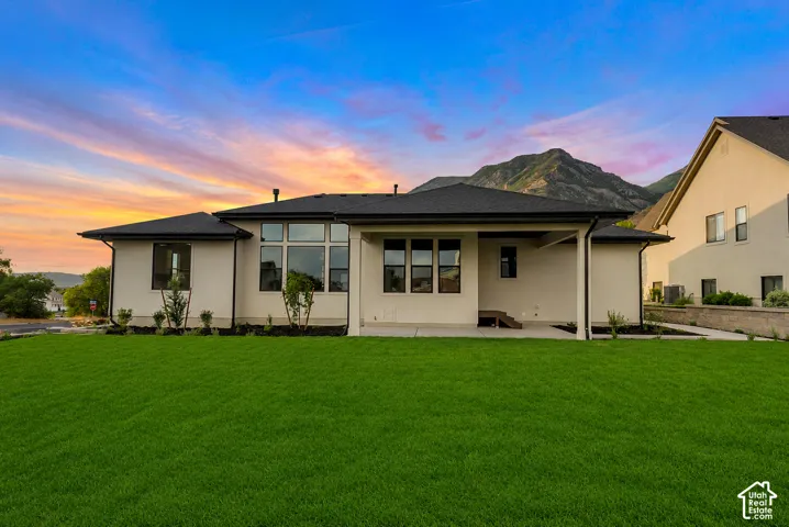 Expansive green lawn bordering a contemporary residence with a dark shingle roof, light-colored stucco exterior, and black-framed windows