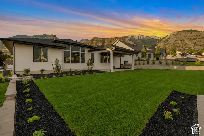 Expansive backyard featuring a manicured lawn, organized landscape beds, and a covered patio