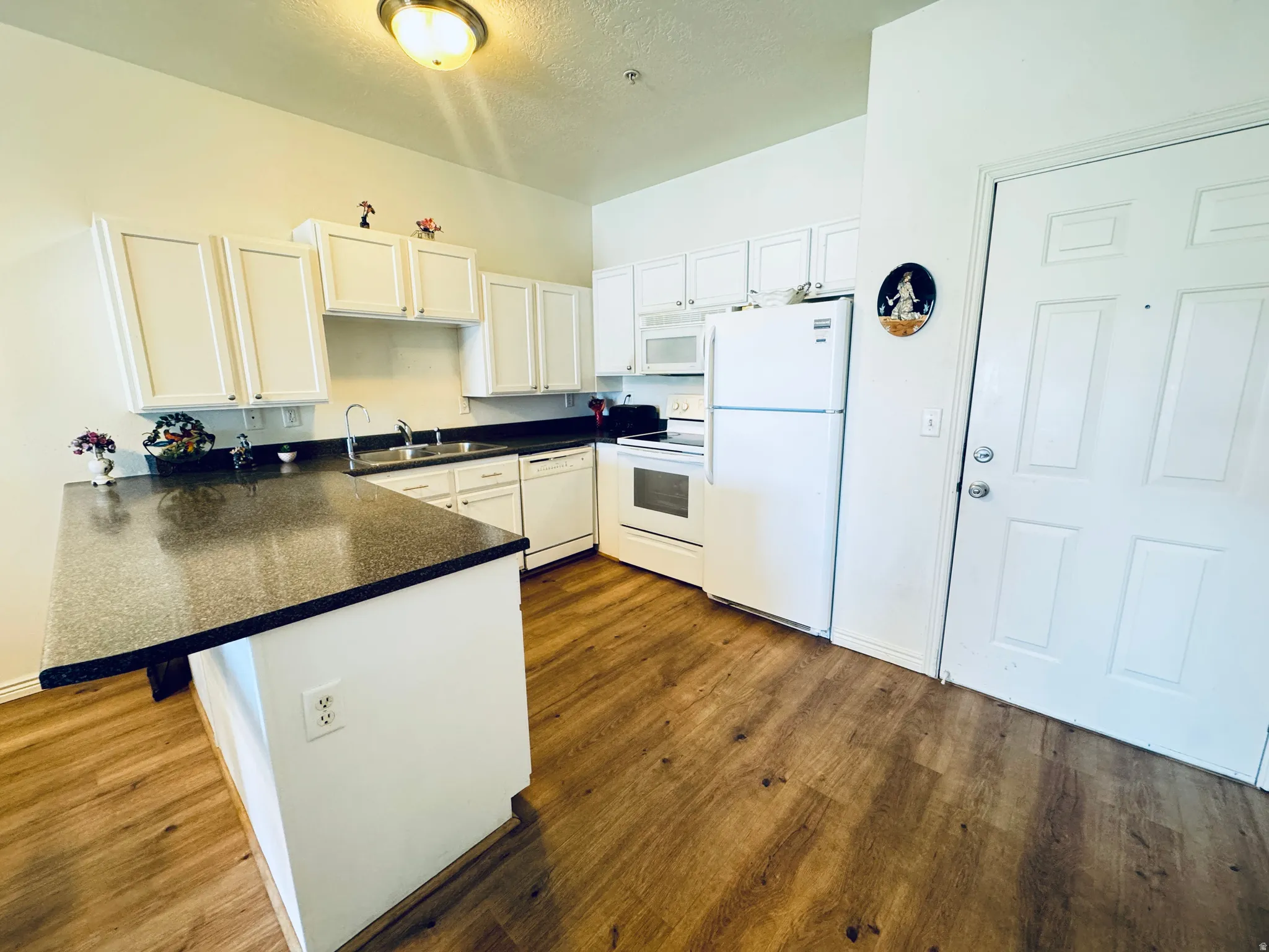 Kitchen with a peninsula, dark countertops, white cabinets, white appliances, and a kitchen bar