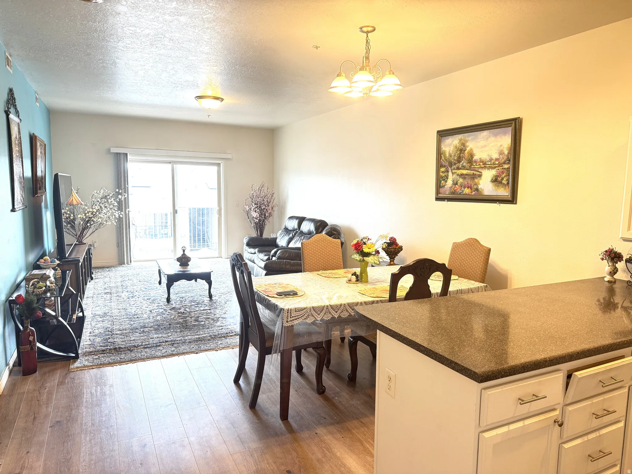 Kitchen, dining area and gathering room featuring light wood-style flooring, a textured ceiling, and a chandelier