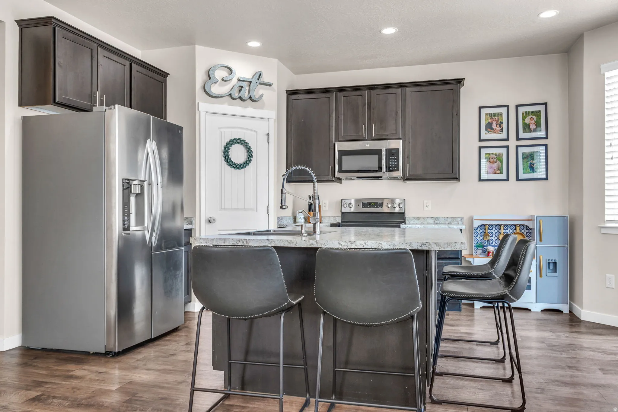 Kitchen featuring stainless steel appliances, dark wood finish cabinetry, an island with sink, dark wood-style flooring, and a kitchen bar