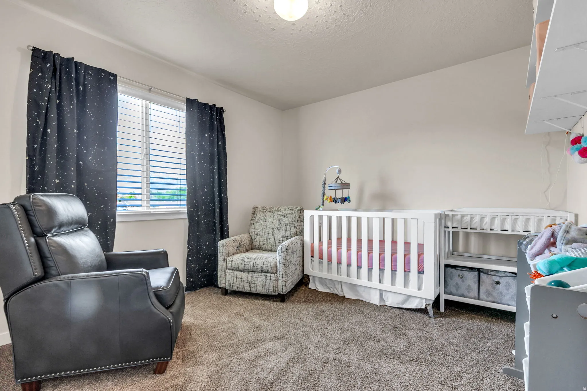 Bedroom with a nursery area, carpet flooring, and a textured ceiling