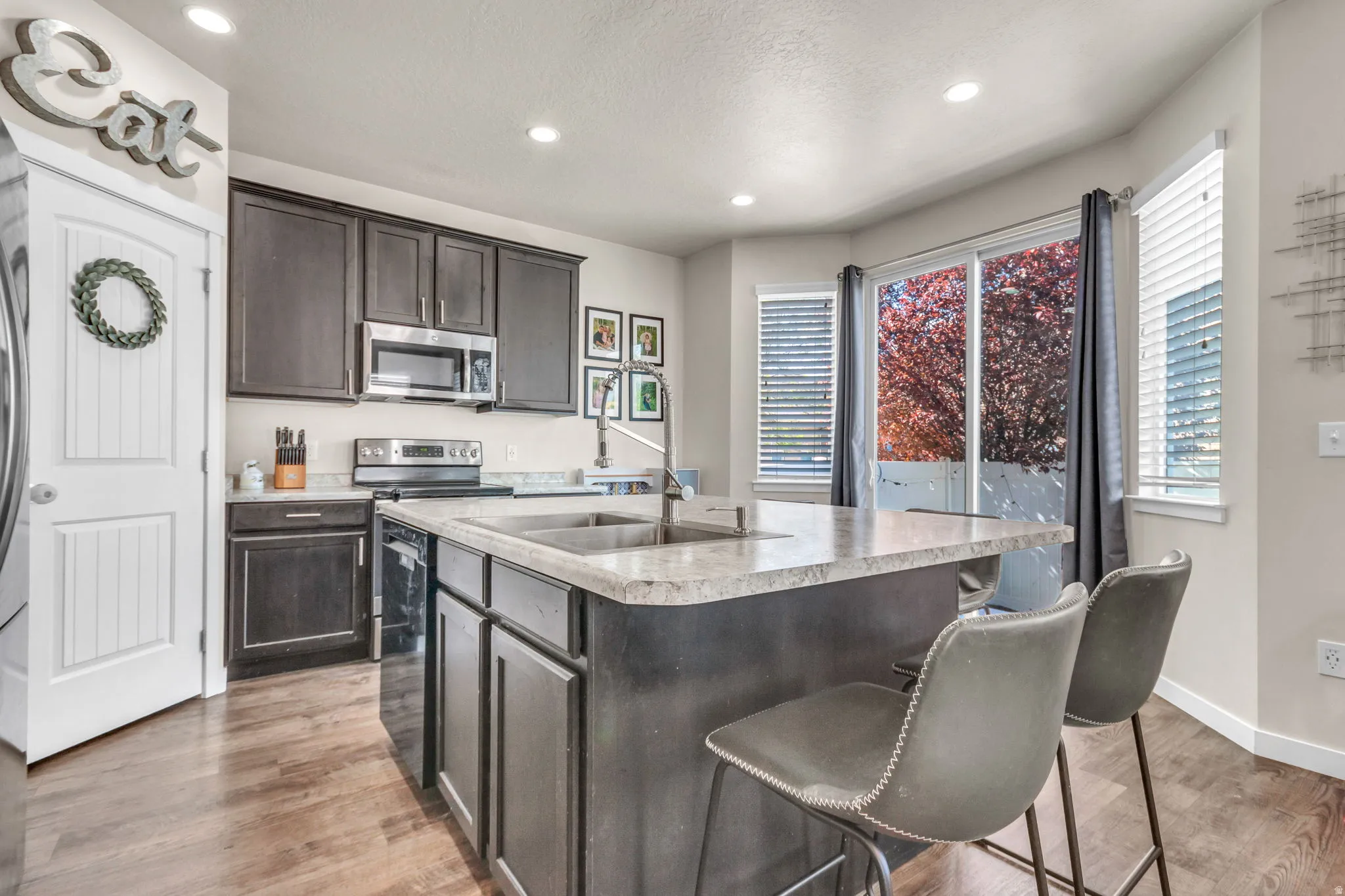 Kitchen with dark wood finish cabinets, light countertops, recessed lighting, a kitchen island with sink, and light wood finished floors