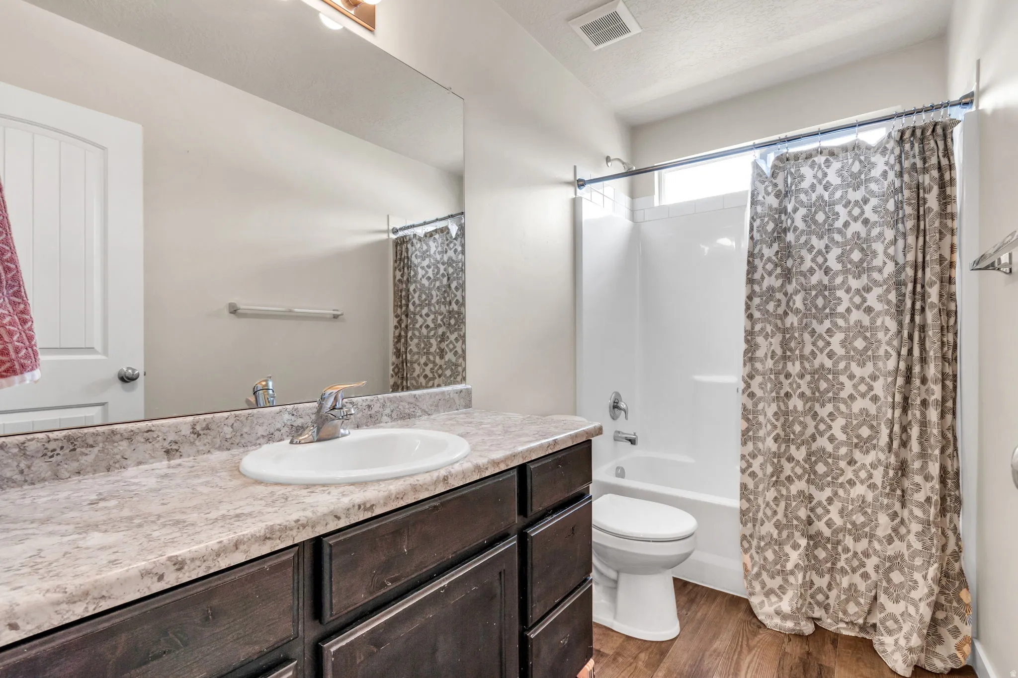 Bathroom featuring vanity, dark wood-style floors, shower / bathtub combination with curtain, and a textured ceiling
