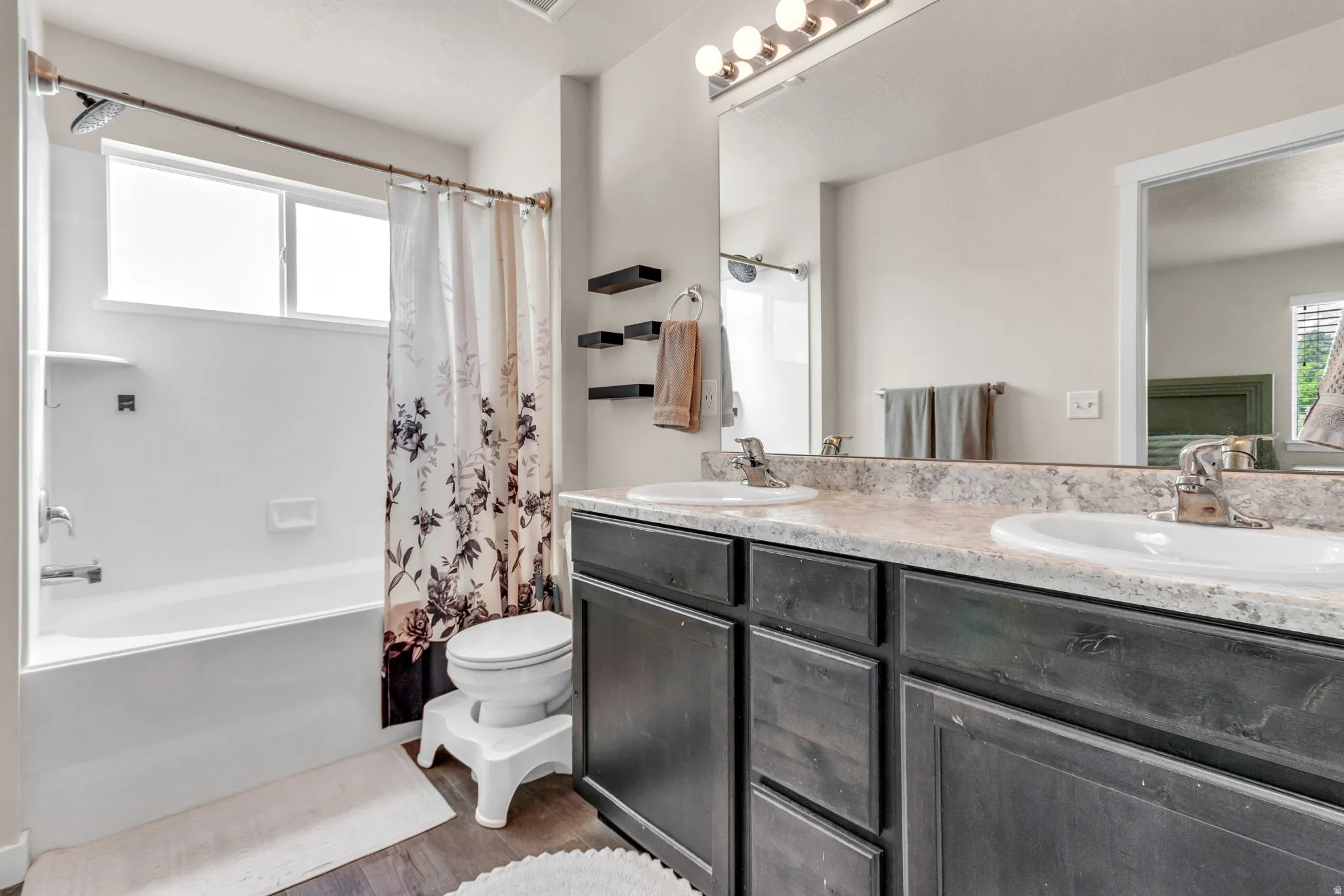 Bathroom featuring double vanity, shower / bath combo with shower curtain, and light wood-type flooring