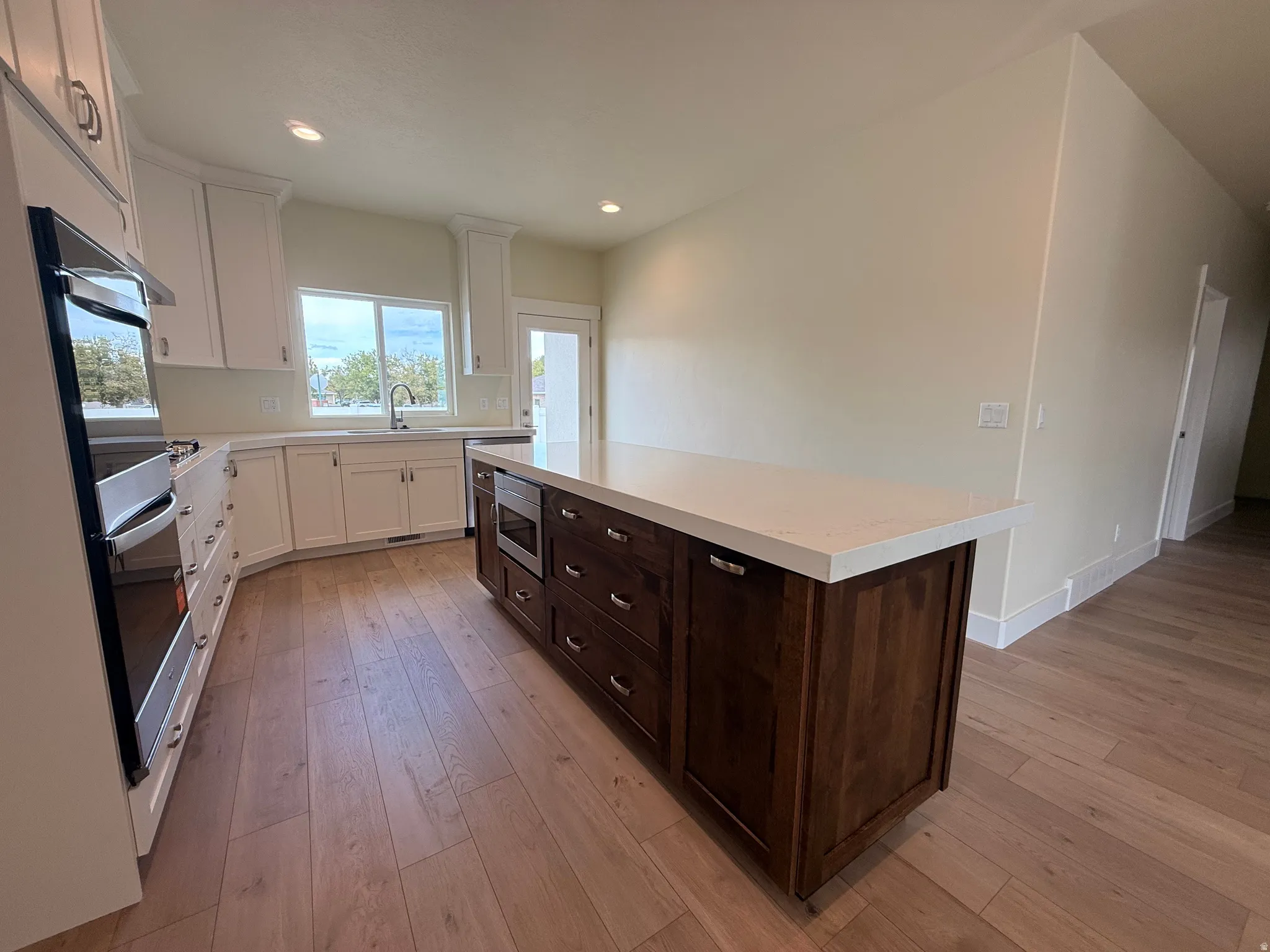 Kitchen featuring wood-finish flooring, white cabinetry, integrated stainless steel appliances, a large center island with a light-toned countertop, and recessed lighting