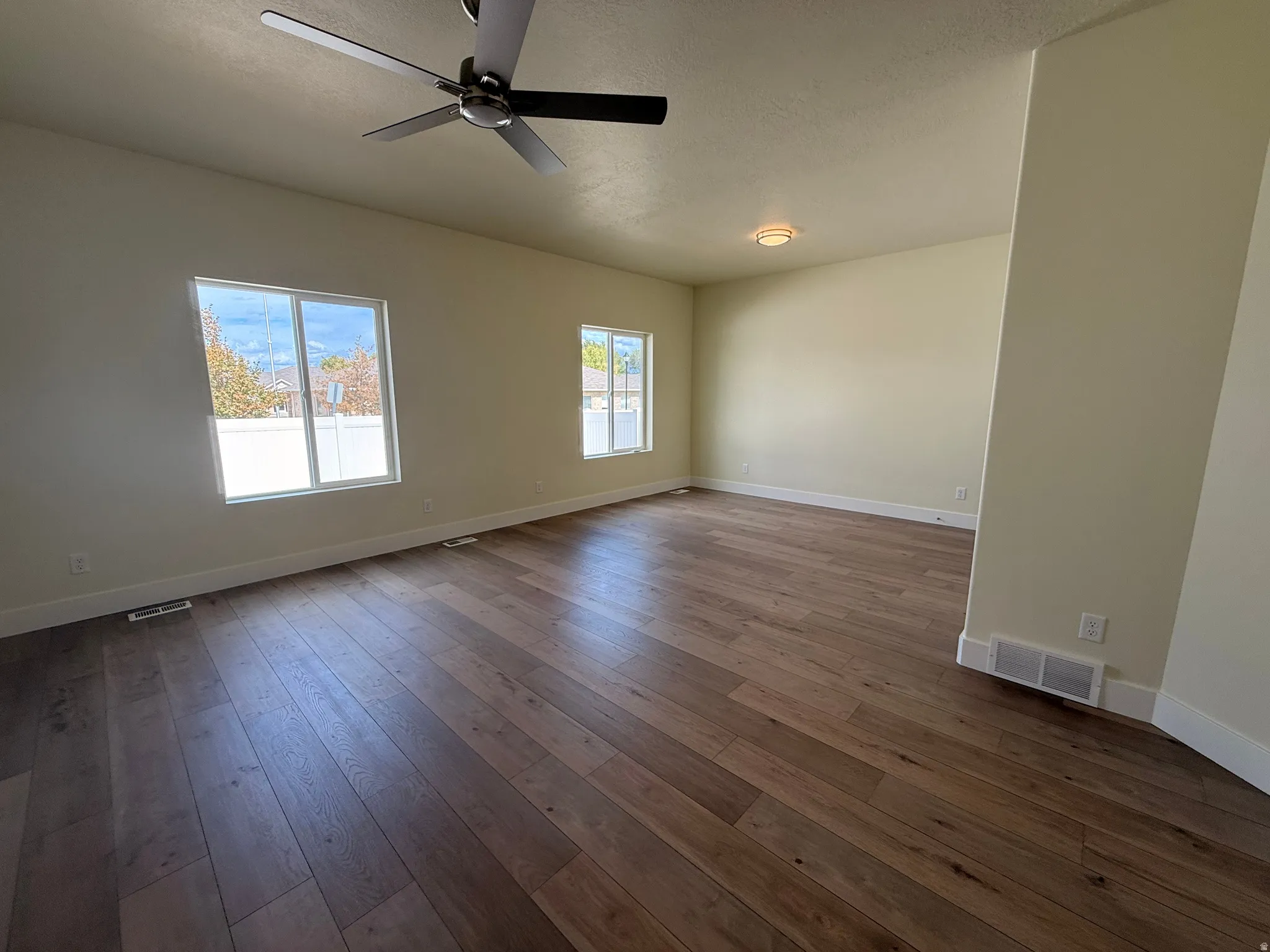 Spacious interior with wood-finish flooring, multiple windows, a ceiling fan, and a flush-mount light fixture
