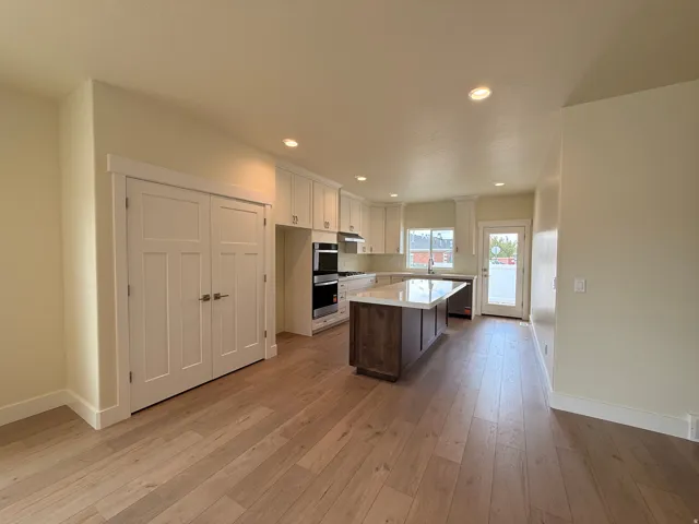Open-concept kitchen with wood-finish flooring, white cabinetry, a central island with a solid surface countertop, and integrated double ovens