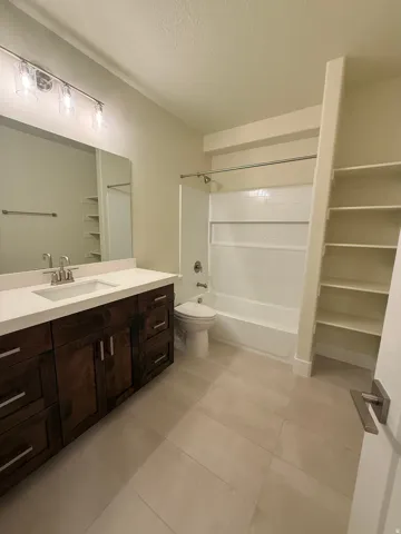 Spacious bathroom featuring a wood-finish vanity with an integrated sink, large mirror, and tiled flooring