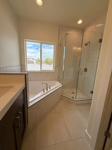 Spacious bathroom featuring a corner soaking tub, glass-enclosed shower, dual sink vanity with quartz countertop, and recessed lighting