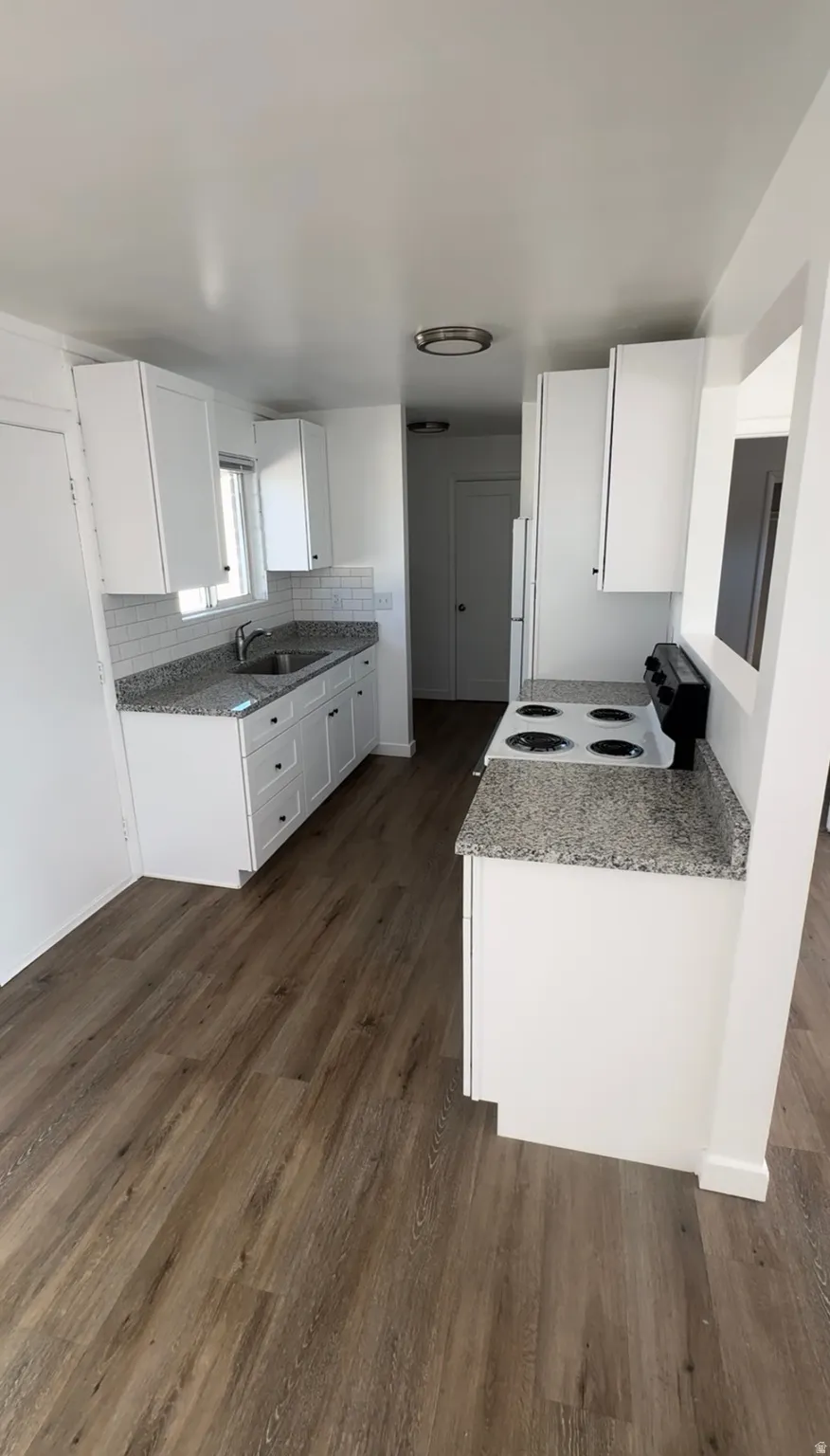 Kitchen with white cabinets, electric range, light stone countertops, and dark wood-style floors