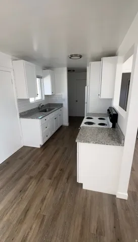 Kitchen with white cabinets, electric range, light stone countertops, and dark wood-style floors