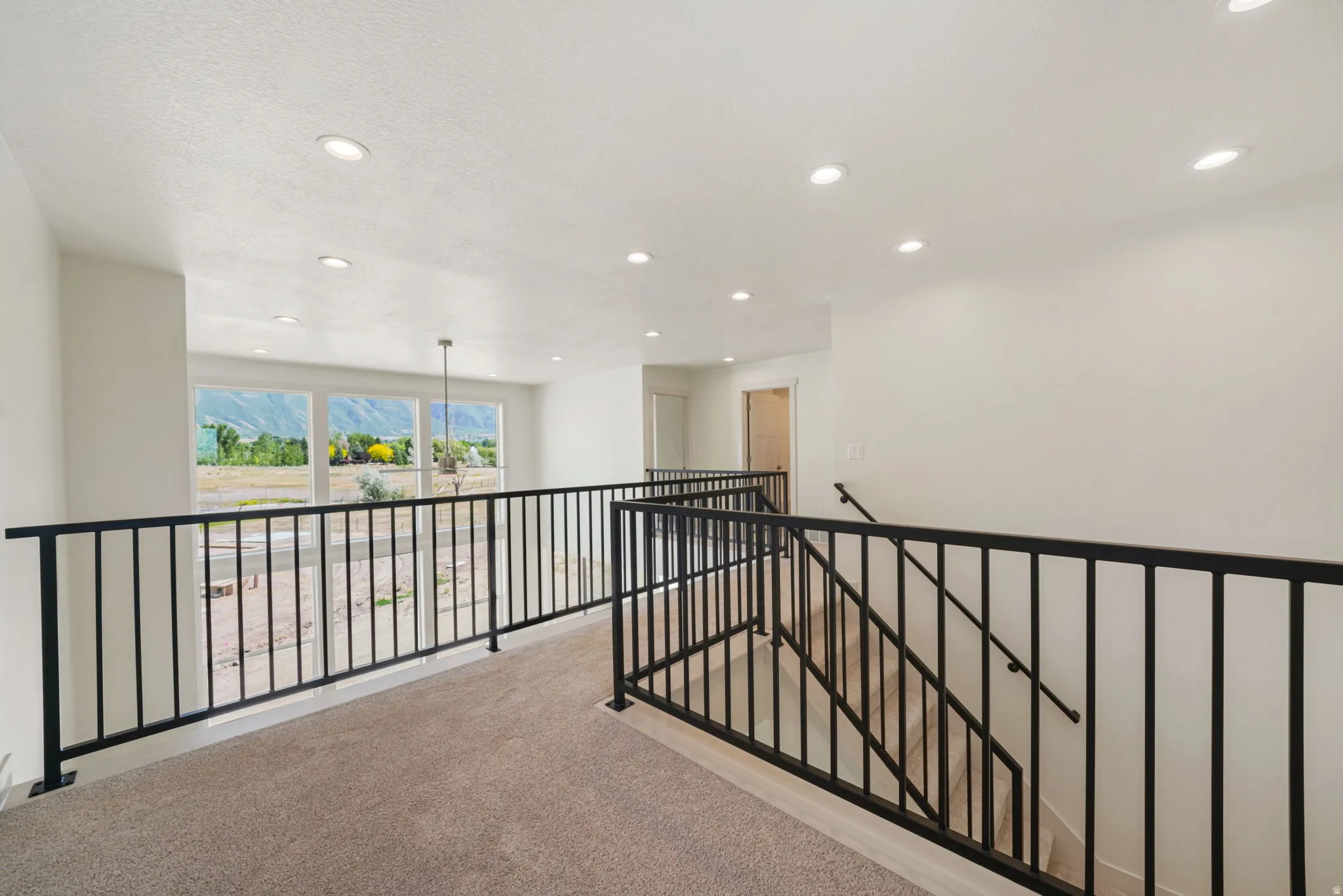 Upper-level landing featuring neutral carpeting, contemporary black metal railings, recessed lighting, and a multi-pane window with mountain scenery
