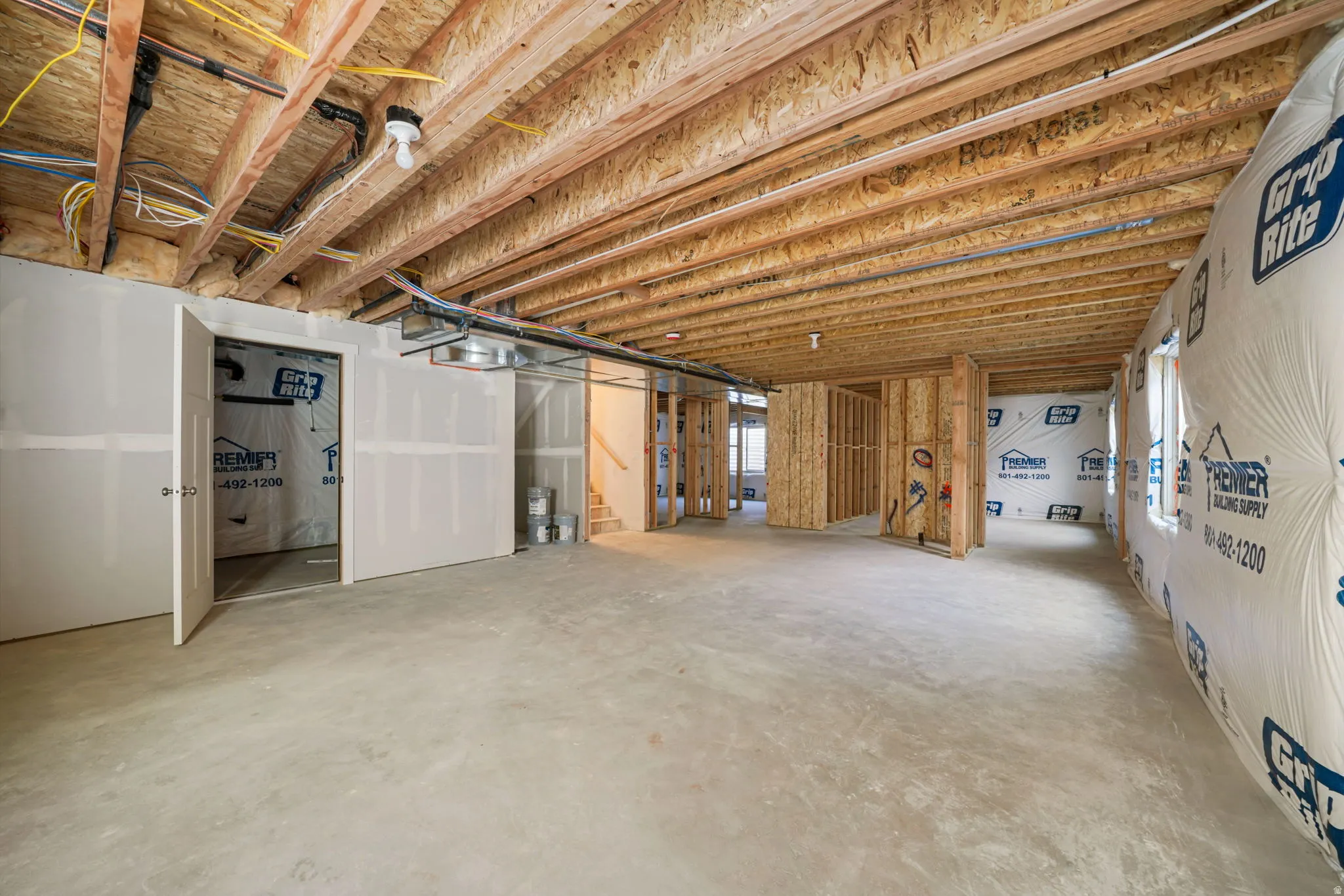 Unfinished basement space featuring exposed wood joists and subflooring, concrete flooring, and partial drywall installation