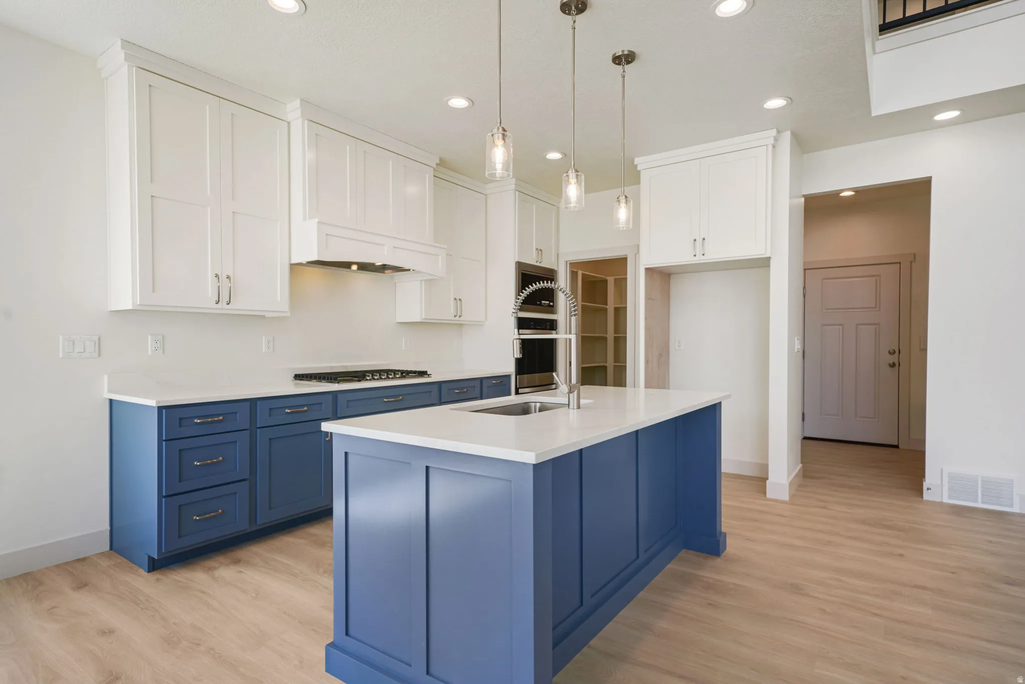 Modern kitchen featuring two-tone cabinetry, a central island with an integrated sink, pendant lighting, a gas cooktop, and wood-finish flooring
