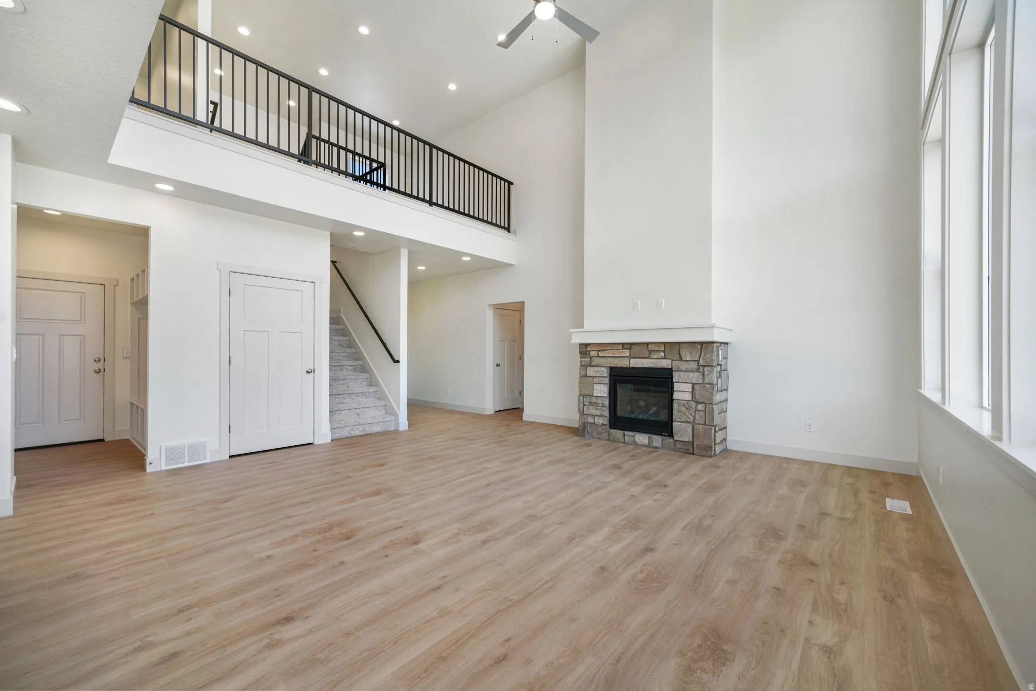 Spacious living area featuring high ceilings, wood-finish flooring, and a stone-clad fireplace