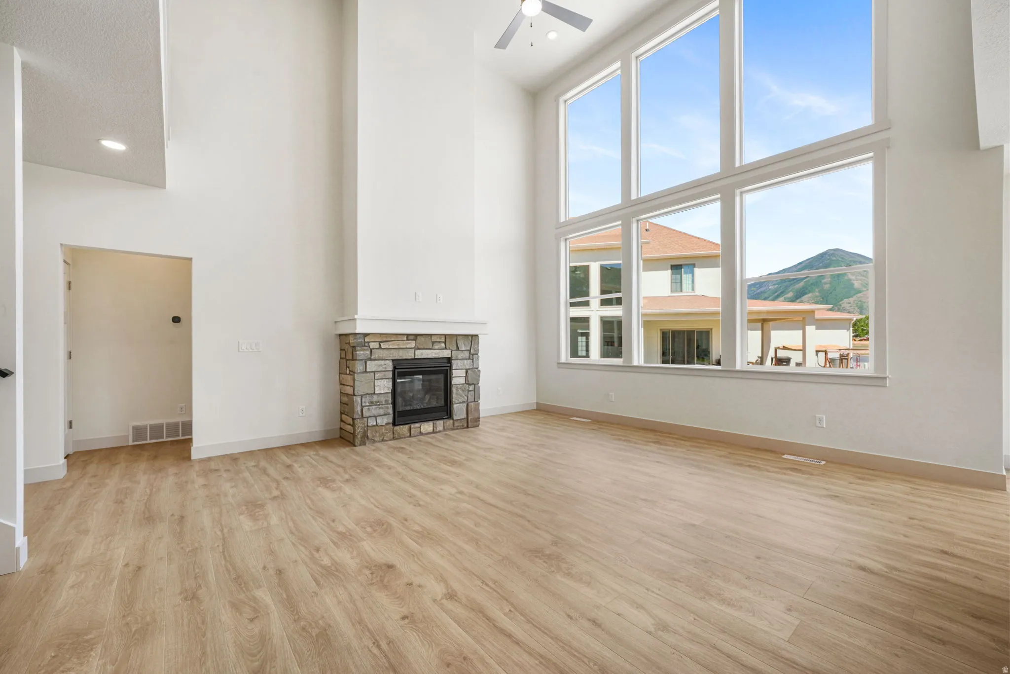 Two-story great room featuring a stone fireplace with a white mantel, expansive window wall, wood-finish flooring, and recessed lighting