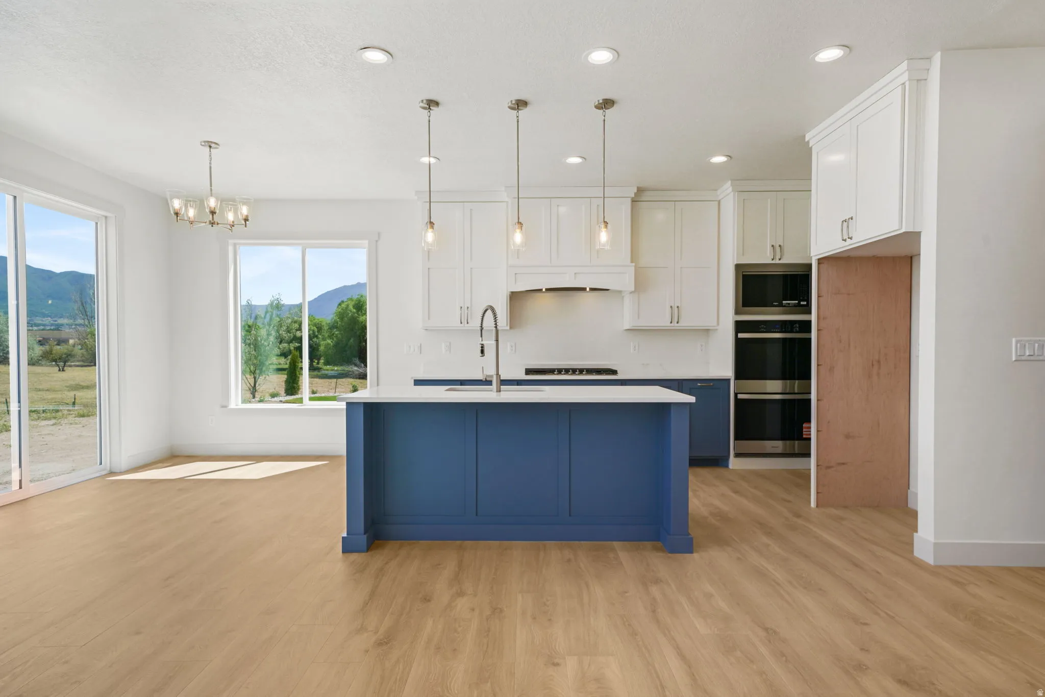 Expansive kitchen featuring a blue island with pendant lighting, white perimeter cabinetry, built-in double ovens, and wood-finish flooring