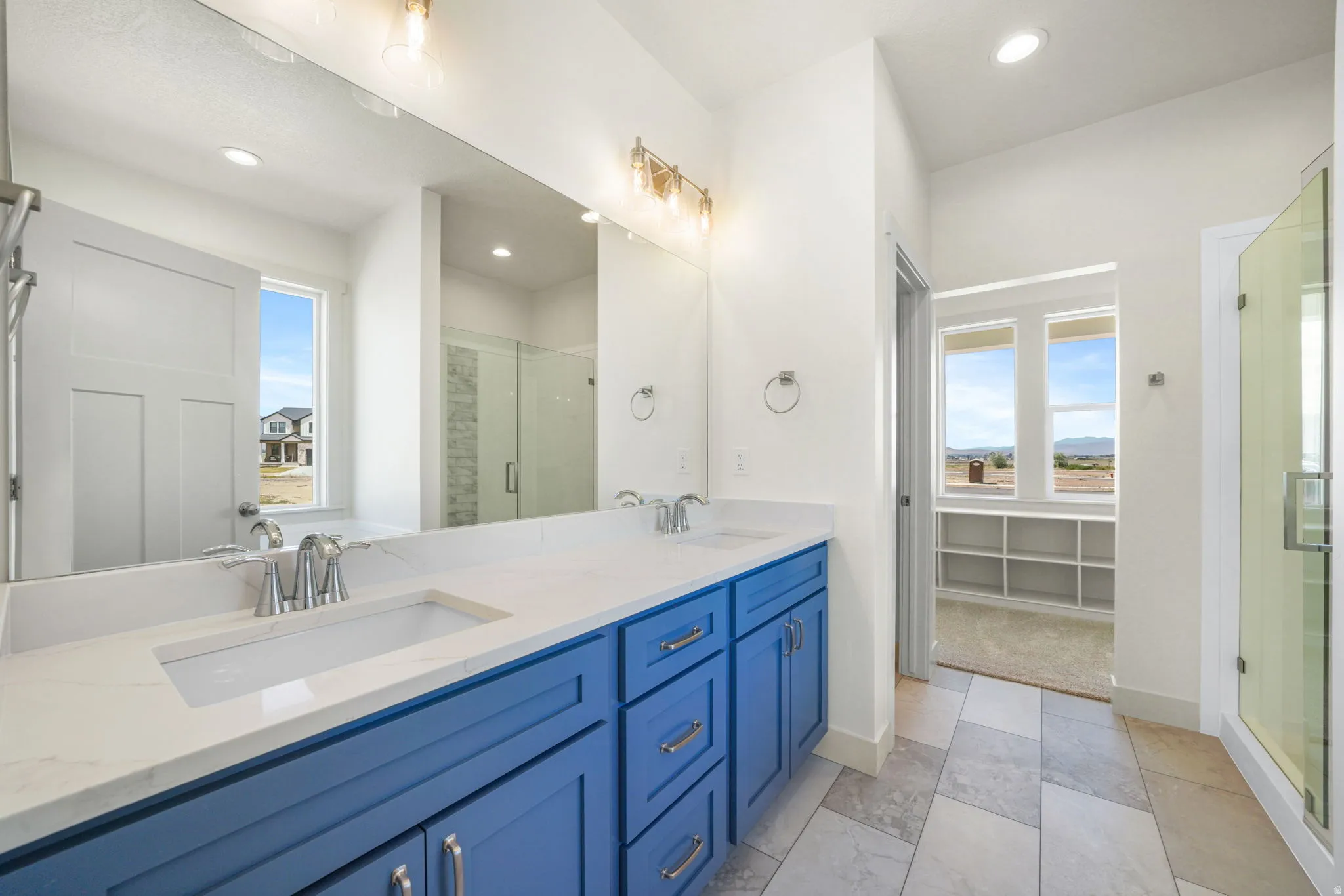 Spacious bathroom featuring a double vanity with blue cabinetry, a large frameless mirror, and a glass-enclosed shower