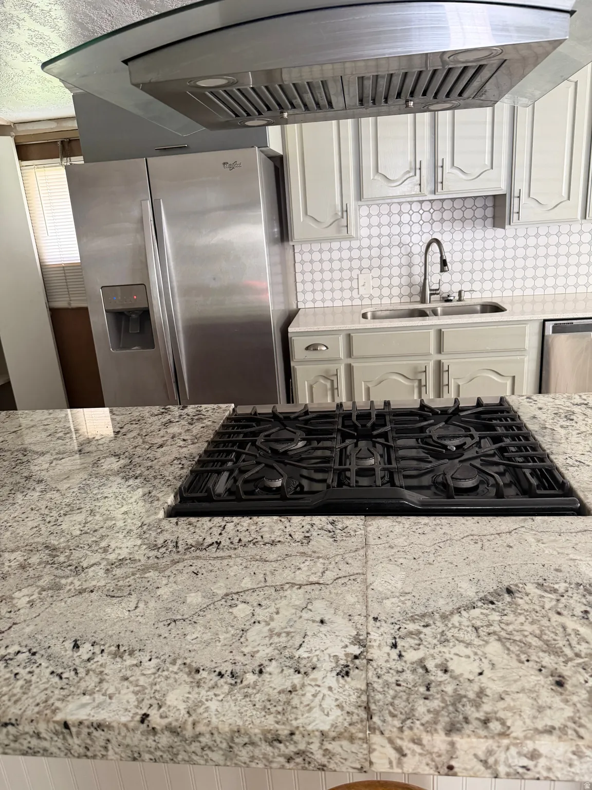 Kitchen with range hood, stainless steel appliances, light stone countertops, and white cabinets