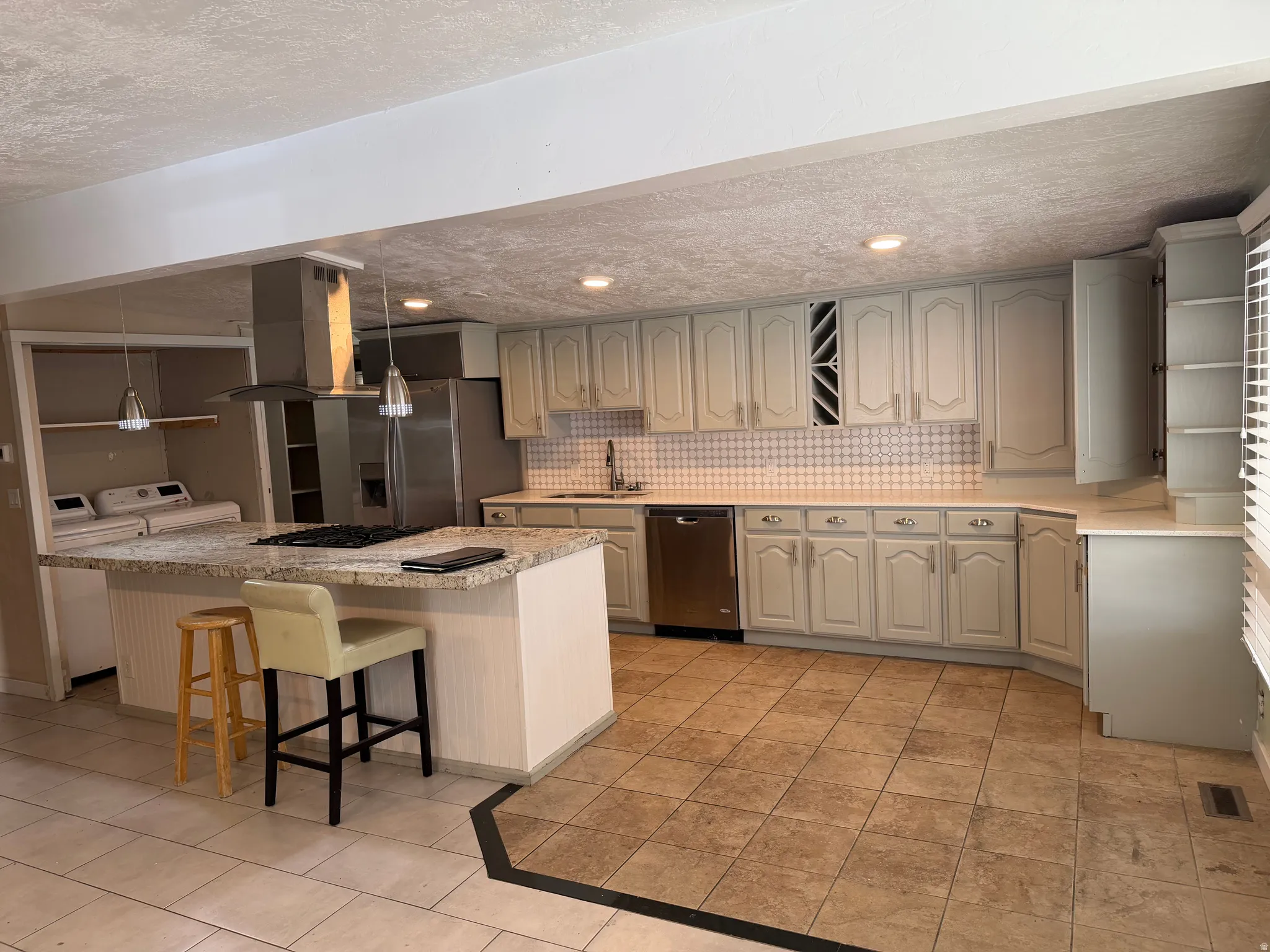 Kitchen with a textured ceiling, a kitchen bar, stainless steel appliances, island range hood, and decorative backsplash