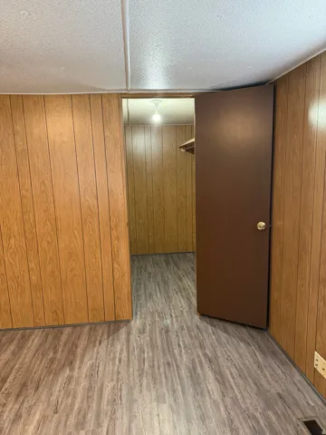 Master walk-in closet with a textured ceiling, wood finished floors, and wood walls