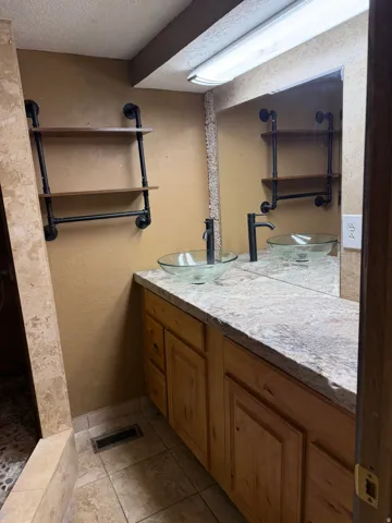 Full bathroom featuring vanity, a textured ceiling, a textured wall, light tile patterned flooring, and walk in shower