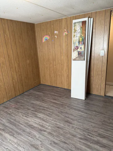 Third bedroom with dark wood-style floors and wooden walls