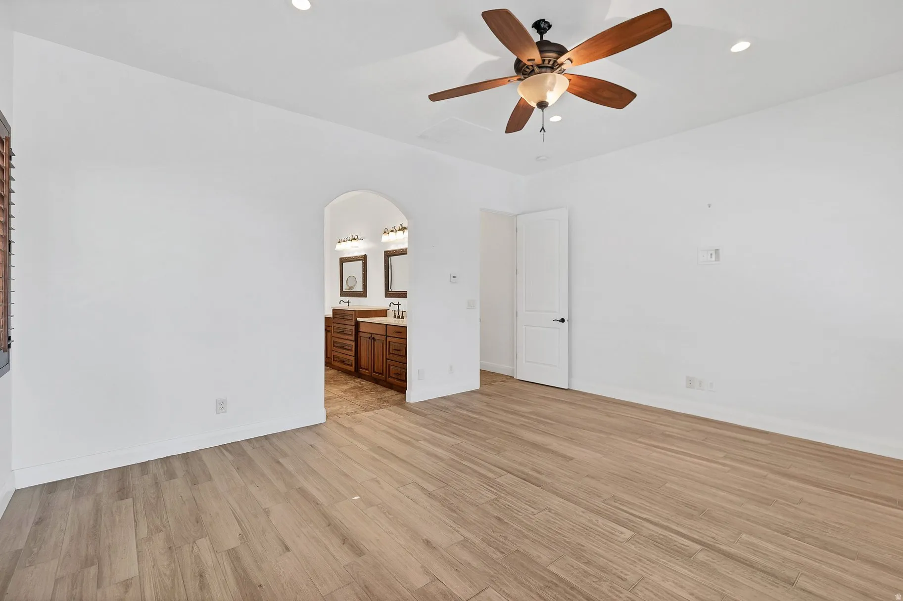 Unfurnished bedroom with light wood finished floors, arched walkways, ceiling fan, recessed lighting, and connected bathroom