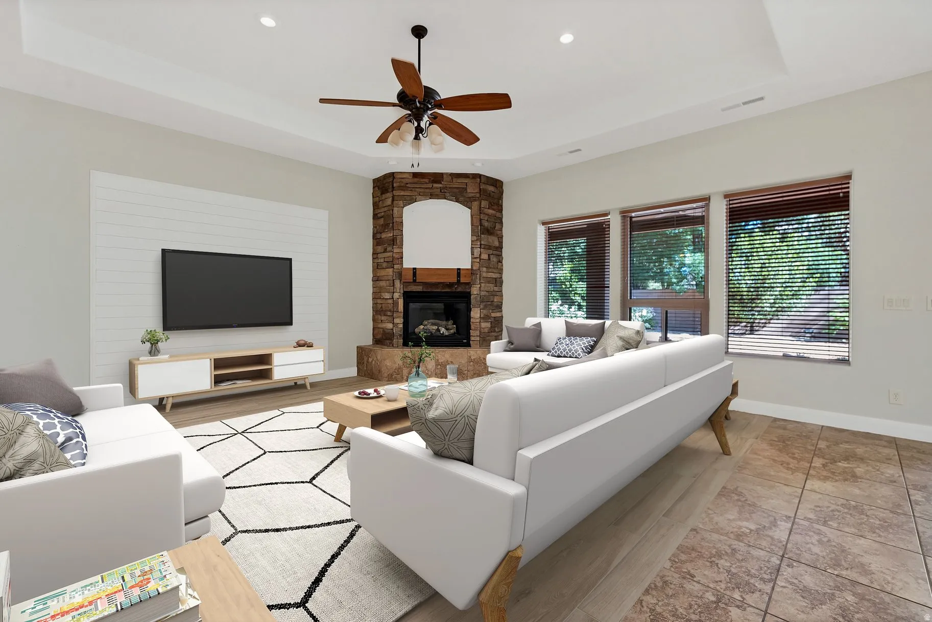 Living area featuring a tray ceiling, ceiling fan, a stone fireplace, recessed lighting, and light wood-style flooring