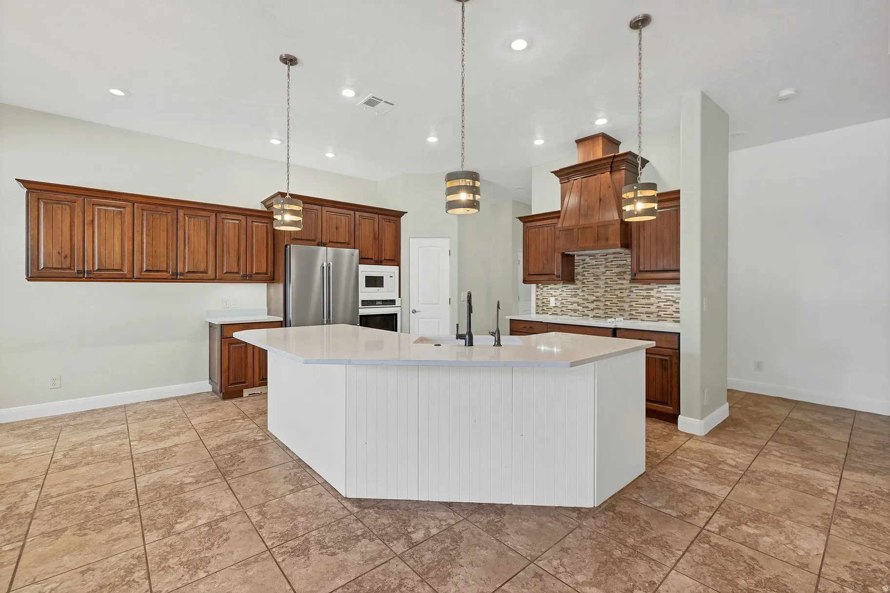 Kitchen with wood finish cabinetry, a large island, white appliances, pendant lighting, and decorative backsplash